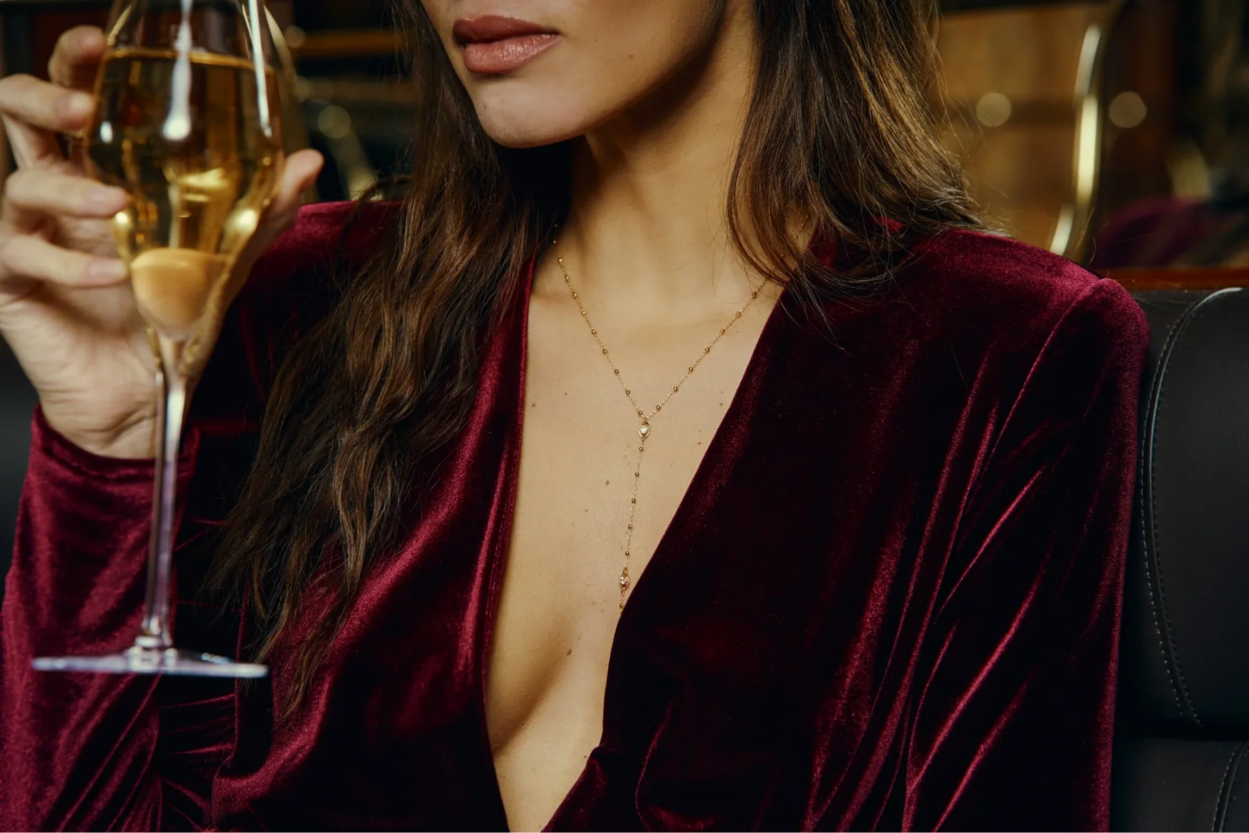 Portrait partiel d'une femme en robe rouge velours mettant en valeur un collier en or raffiné et un verre de champagne